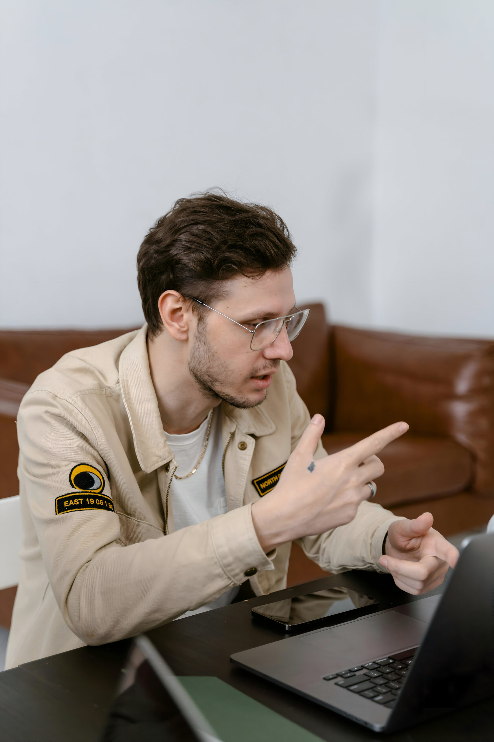 A young man in a beige jacket and glasses points at a laptop screen while discussing digital marketing strategies for businesses in Siliguri.